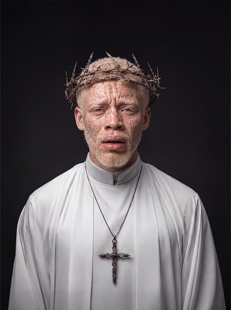 Portrait of a man dressed in white wearing a crown of barbed wire and a matching cross, exploring martyrdom, sacrifice, faith and resilience through contemporary fine art.